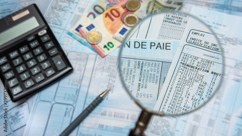 Bulletin de paie français à la loupe, avec argent liquide en euros, calculette et stylo photo
