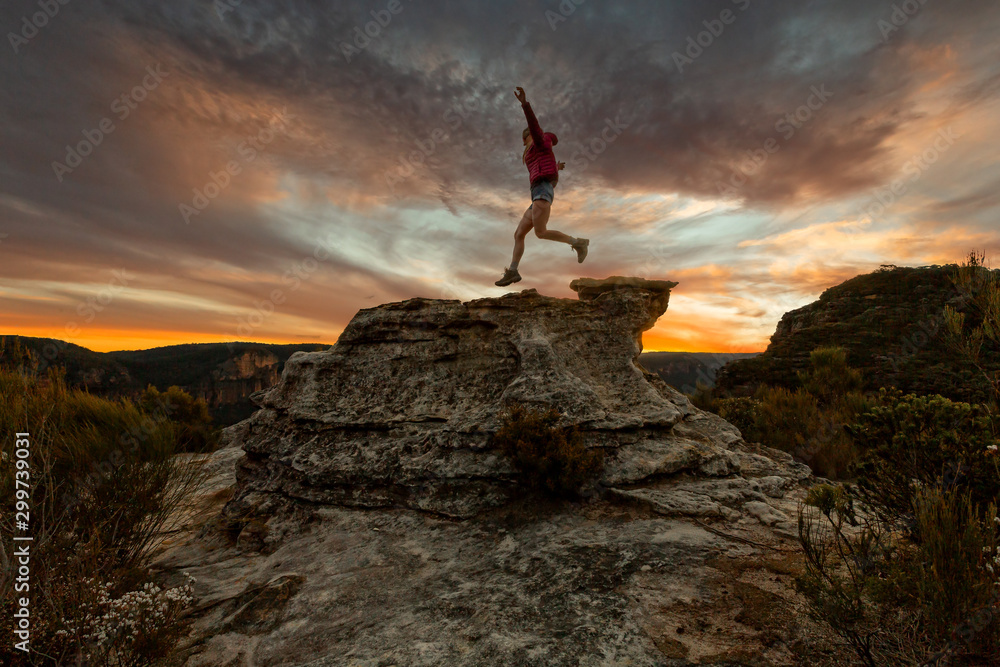 Active woman jumping on mountain cliffs at sunset