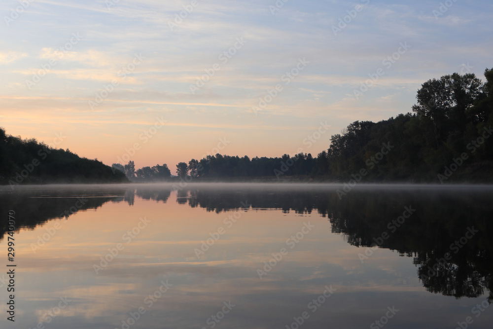 Beautiful calm sunrise dawn by the river with reflection on mirror water. Nice pastel colors nature landscape. Trees silhouette, fog, clouds and sunset photo.