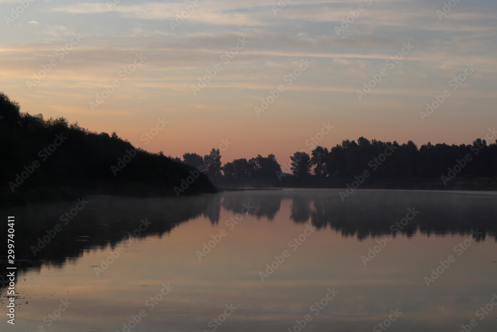 Beautiful calm sunrise dawn by the river with reflection on mirror water. Nice pastel colors nature landscape. Trees silhouette, fog, clouds and sunset photo.