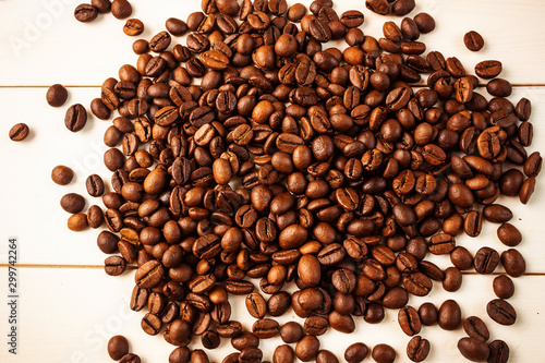 Coffee beans scattered on a light wooden background. The concept of growing and making coffee. Top view, minimalism.