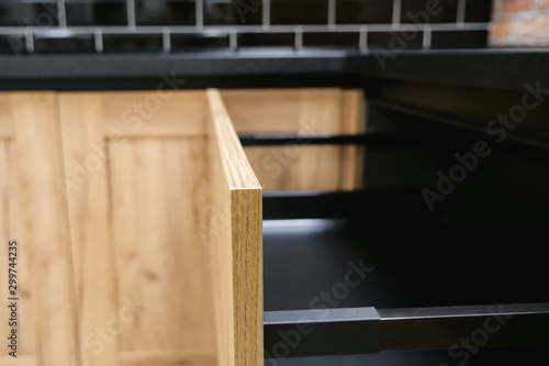 empty drawer made of black metal and wooden front panel in modern kitchen set against brick wall extreme close view