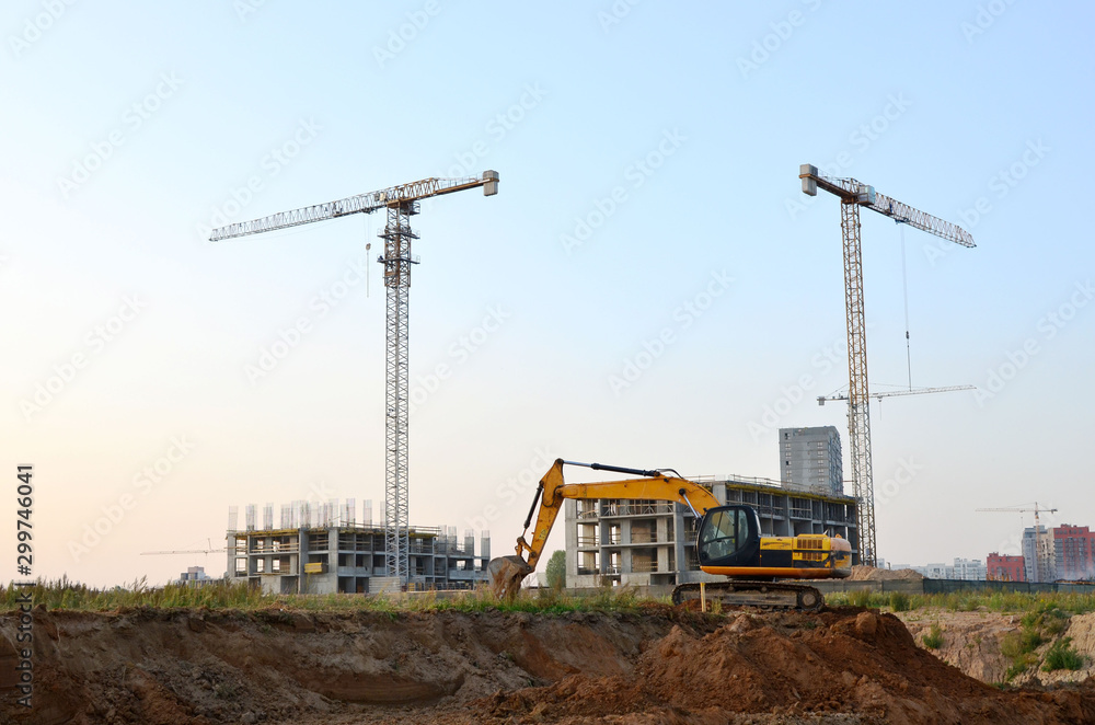 Excavator digs the ground for the foundation and construction of a new building. Laying or replacement of underground sewer pipes. Tower cranes at construction site, renovation program Excavator digs the ground for the foundation and construction of a new building. Laying or replacement of underground sewer pipes. Tower cranes at construction site, renovation program