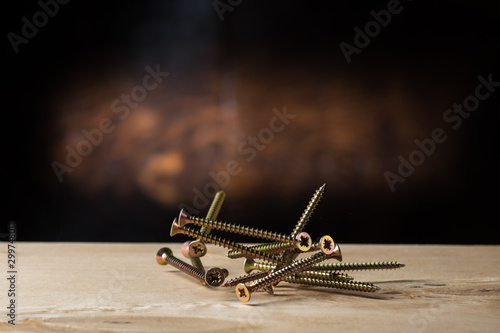 self-tapping screws falling on plywood on a wood background, black, chromed and yellow