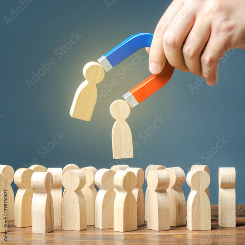 Foto Businessman with a magnet pulls wooden figures of people out of big crowd
