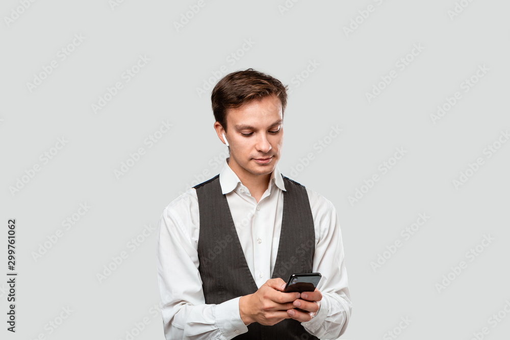 Young businessman in a white shirt and grey vest looking at the screen of a smartphone. Young businessman in a white shirt and grey vest looking at the screen of a smartphone.