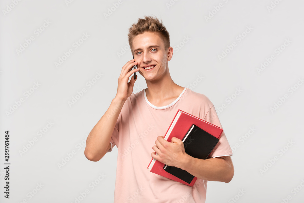 Handsome young man in a pink t-shirt with books and files talking on the phone. Handsome young man in a pink t-shirt with books and files talking on the phone.
