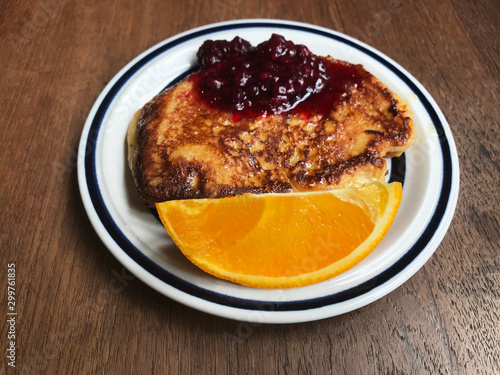 French toast with orange and red berries on white plate, top view.