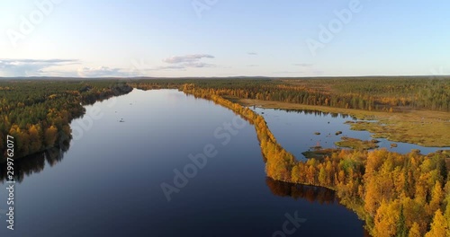 River in Lapland,  Aerial, tracking, drone shot, panning around a esker on the Almansuvanto stream, surrounded by foliage color forest at golden hour, on a sunny, fall evening, in Sodankyla, Finland photo