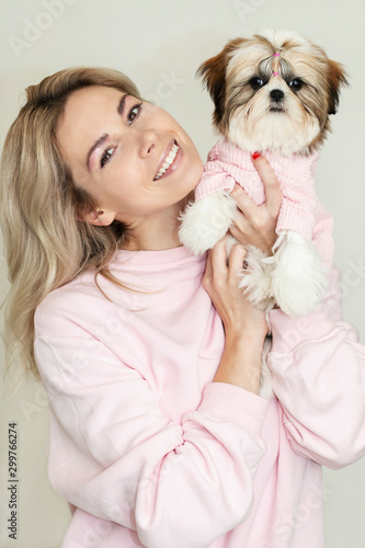 beautiful blonde girl with a cute shih tzu puppy in pink clothes on a light background