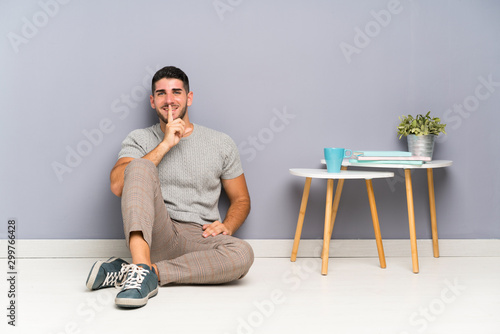 Young handsome man sitting on the floor doing silence gesture