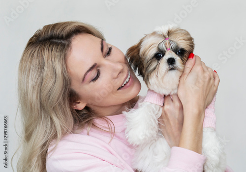 beautiful blonde girl with a cute shih tzu puppy in pink clothes on a light background