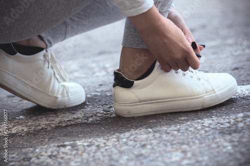 girl squatted down to tie shoelaces on white sneakers on asphalt road  autumn sport concept outdoors