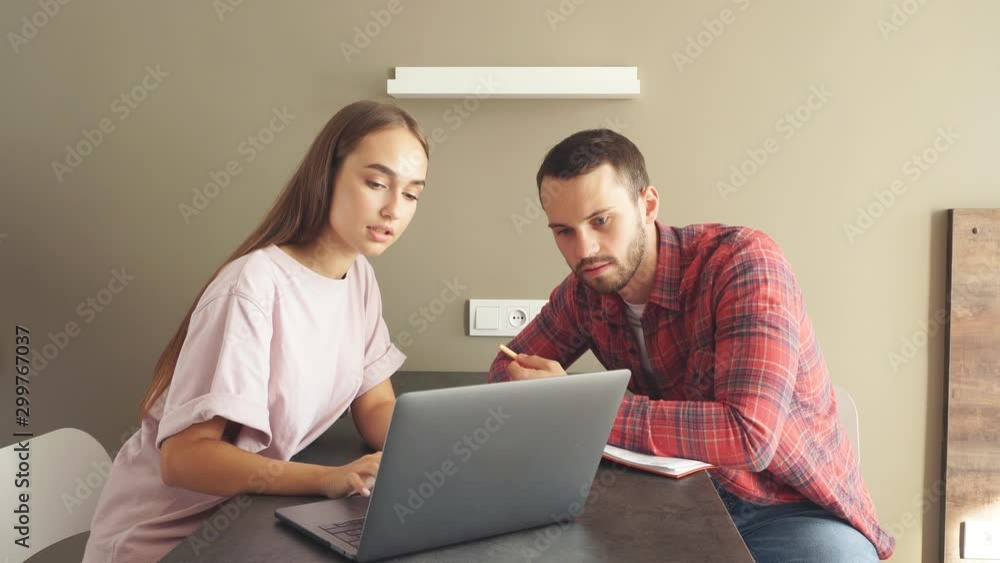 Lovely young couple talking in bright bedroom, sitting at darktable, discussing daily routine job using laptop, family concept Lovely young couple talking in bright bedroom, sitting at darktable, discussing daily routine job using laptop, family concept
