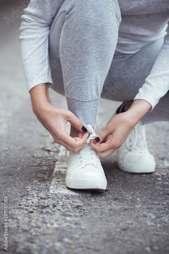 girl squatted down to tie shoelaces on white sneakers on asphalt road, autumn sport concept outdoors