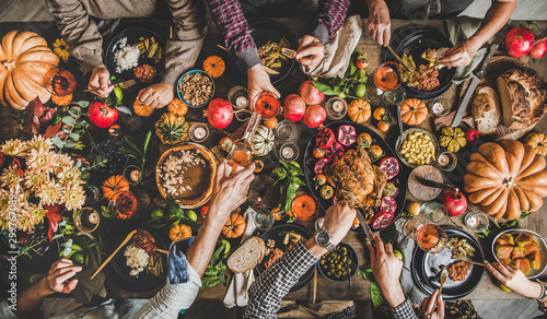 Family celebrating Thanksgiving day. Flat-lay of eating and pouring wine peoples hands over Friendsgiving table with traditional Fall food, roasted turkey, candles, pumpkin pie, top view