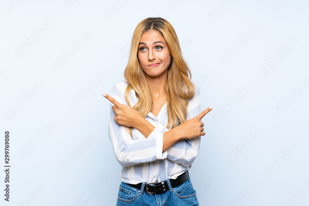 Young blonde woman over isolated blue background pointing to the laterals having doubts Young blonde woman over isolated blue background pointing to the laterals having doubts