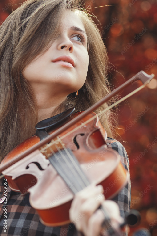 autumn portrait beautiful woman enjoying playing violin on a background of red leaves, romantic girl engaged in art on nature, concept of hobby and music lifestyle