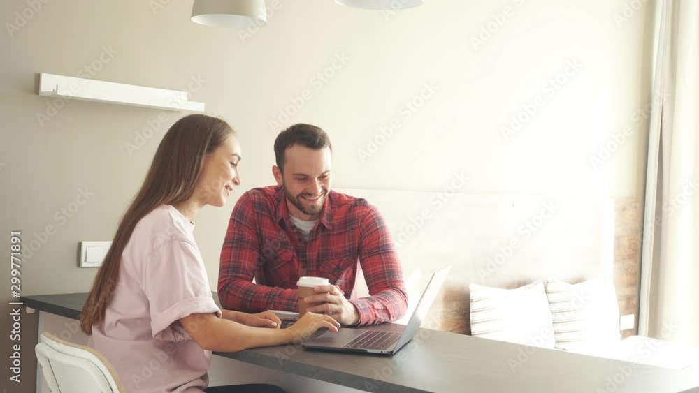 Handsome man together with beautiful young woman spending time in front of laptop computer, staring at screen with positive emotions Handsome man together with beautiful young woman spending time in front of laptop computer, staring at screen with positive emotions