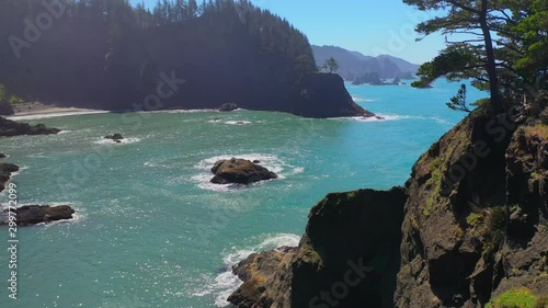 Aerial: Drone reversing over rocky coastline in sea against blue sky on sunny day - Southern Coast, Oregon