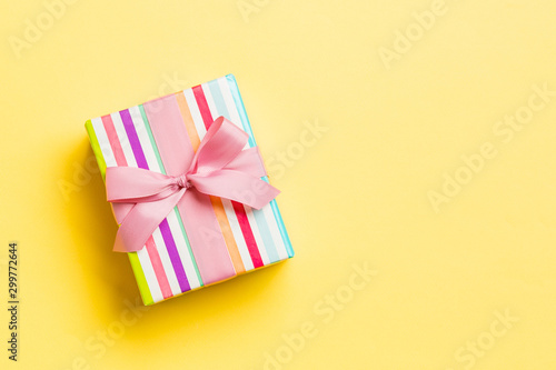 wrapped Christmas or other holiday handmade present in paper with pink ribbon on yellow background. Present box, decoration of gift on colored table, top view with copy space