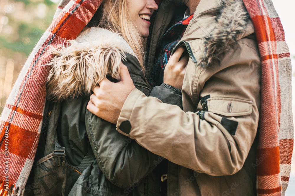 Couple huggings travelers covered with plaid in the forest. Concept of trekking, adventure and seasonal vacation. Couple huggings travelers covered with plaid in the forest. Concept of trekking, adventure and seasonal vacation.