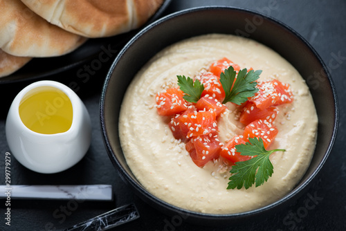 Hummus with slices of salmon, sesame seeds, parsley and olive oil in a black bowl, elevated view