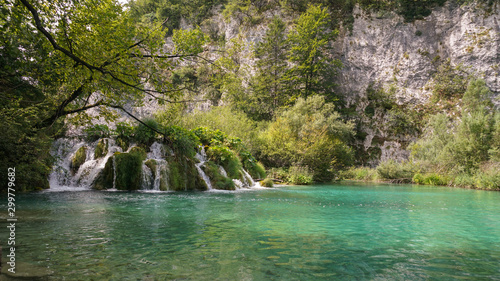 A bunch of bubbling and noisy waterfalls is surrounded by cliffs overgrown with forest.