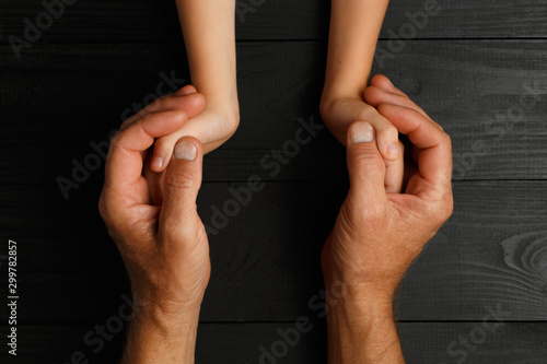 Hands of an elderly man holding the hand of a younger man.