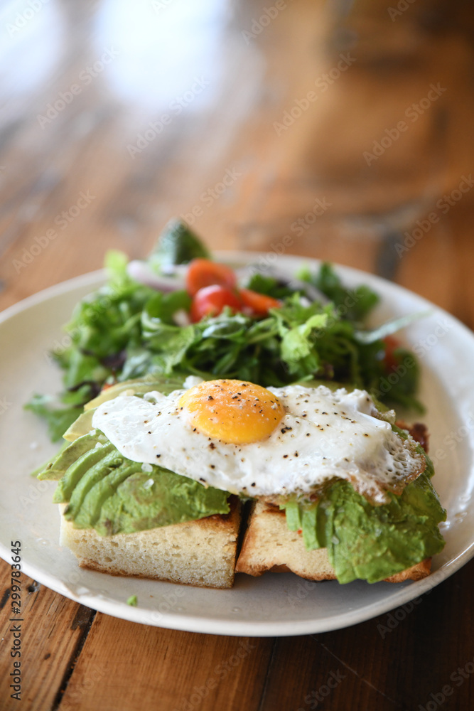 Avocado and fried egg brioche with salad served on plate Avocado and fried egg brioche with salad served on plate