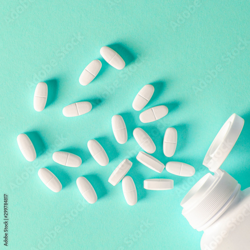 A white plastic container with white tablets lies on a multi-colored background next to white tablets