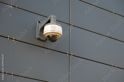 One white-grey surveillance camera on grey metal wall photo