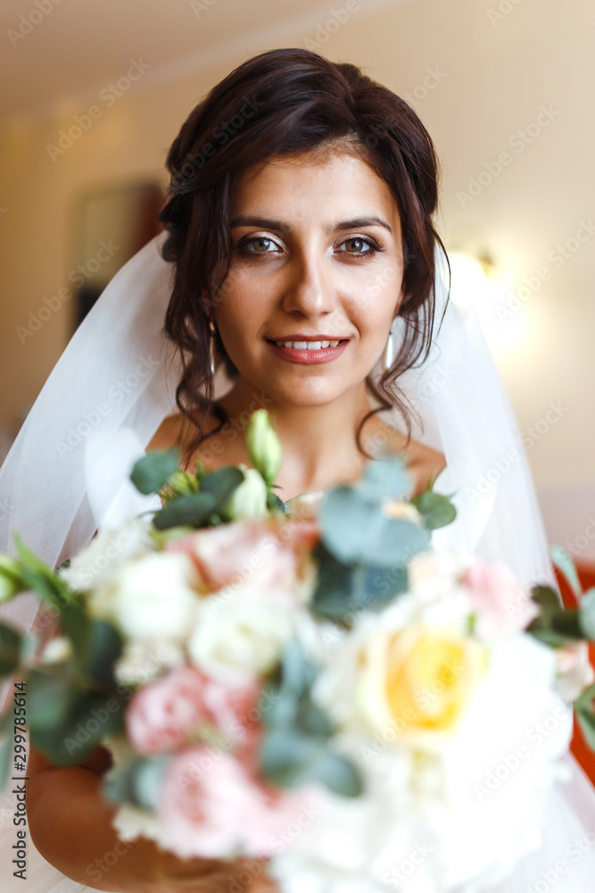 Morning of the bride. Beautiful smiling brunette bride in a white dress with a wedding bouquet in her hands. Elegant woman with professional make up and hair style. Wedding morning of the bride. Morning of the bride. Beautiful smiling brunette bride in a white dress with a wedding bouquet in her hands. Elegant woman with professional make up and hair style. Wedding morning of the bride.