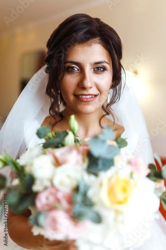 Morning of the bride. Beautiful smiling brunette bride in a white dress with a wedding bouquet in her hands. Elegant woman with professional make up and hair style. Wedding morning of the bride. 