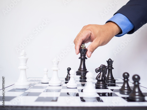 Businessman hand moving king chess piece on board with white background, challenges planning business strategy to success concept