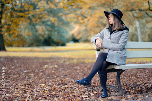 Slika na platnu Young girl in a hat sitting on a bench in the autumn park