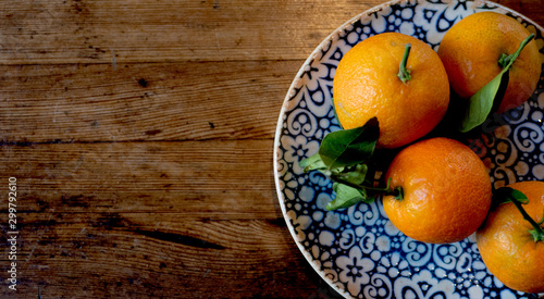 Orange fruits with leaves in a beautiful plate on a wooden table.