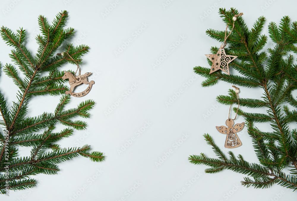 Obraz premium Christmas composition. The border is made of spruce branches, wooden toys in the form of an angel, a star and a rocking horse on a white background. Christmas, winter, New year.