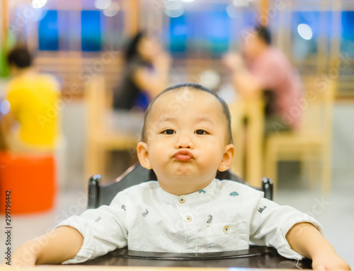 Portrait of adorable baby boy with funny hungry face sitting on table in restaurant while waiting for food.