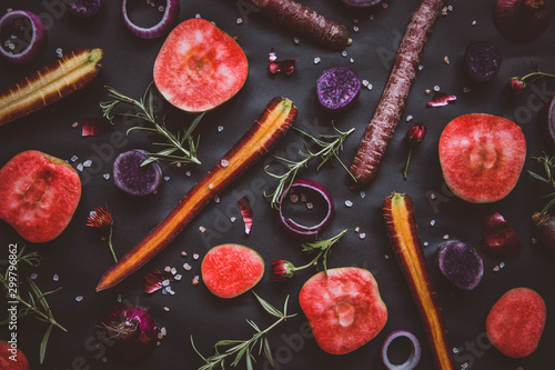 Fruit and vegetable collage on black background: red moon apples, onion rings, purple haze carrots, rosemary