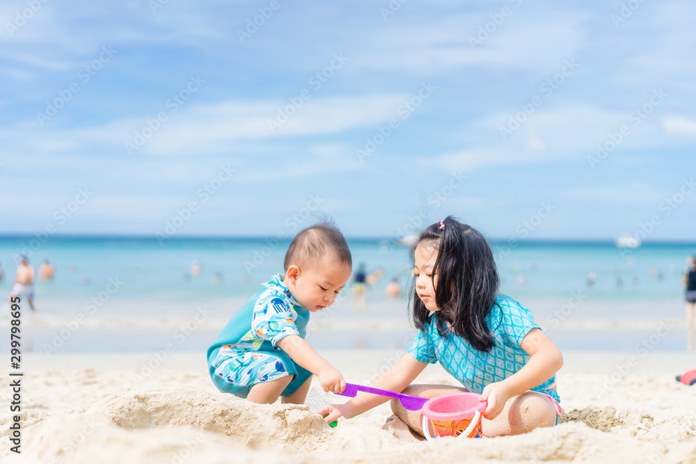 4 years old Little asian girl playing on the beach with her 1 year old baby brother.Children in nature with beautiful sea, sand and blue sky.Happy kids on vacations at seaside Sibling on Vacation. 4 years old Little asian girl playing on the beach with her 1 year old baby brother.Children in nature with beautiful sea, sand and blue sky.Happy kids on vacations at seaside Sibling on Vacation.