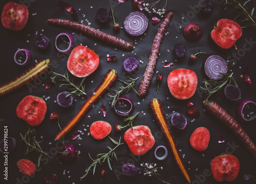 Fruit and vegetable collage on black background: red moon apples, purple haze carrots, onion rings, rosemary