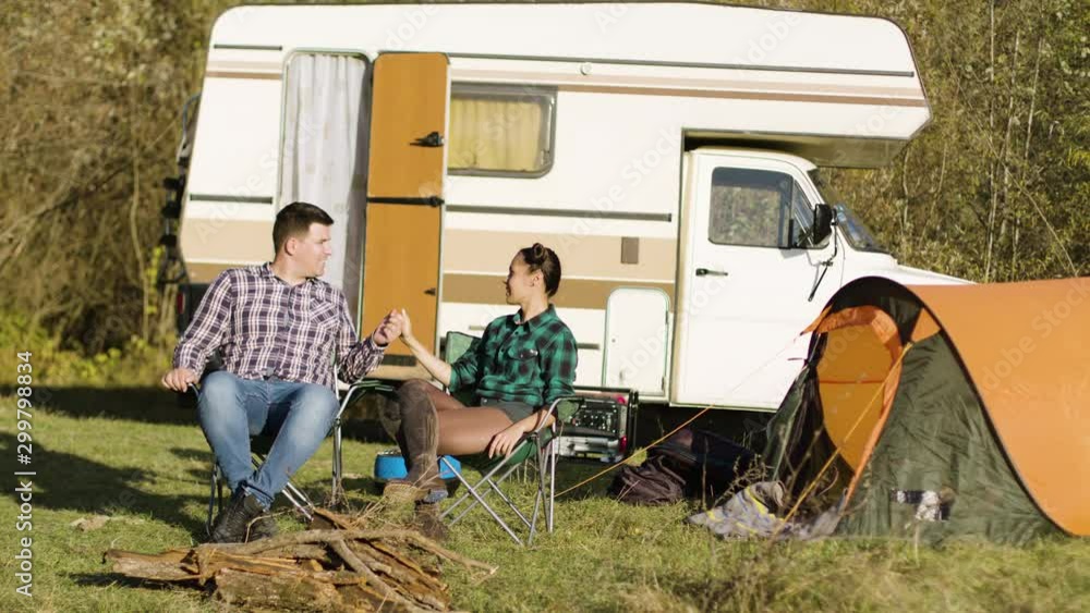 Hipster boyfriend kissing his girlfriend hand while sitting on camping seats Hipster boyfriend kissing his girlfriend hand while sitting on camping seats