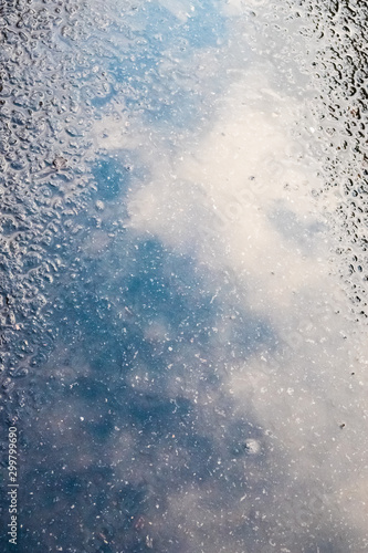 reflection of the blue sky with clouds in a puddle on the pavement