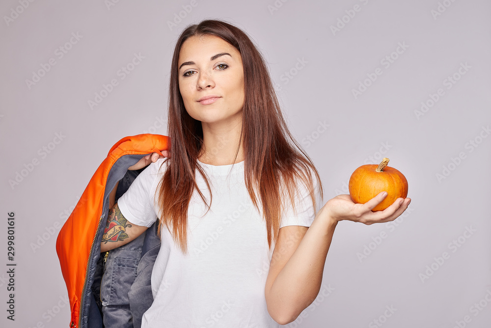 Strong and confident young woman with dark long hair holds vegetable, going to make tasty eco salad, looking at camera, holds orange jumper, has healthy eating, isolated over grey studio background. Strong and confident young woman with dark long hair holds vegetable, going to make tasty eco salad, looking at camera, holds orange jumper, has healthy eating, isolated over grey studio background.
