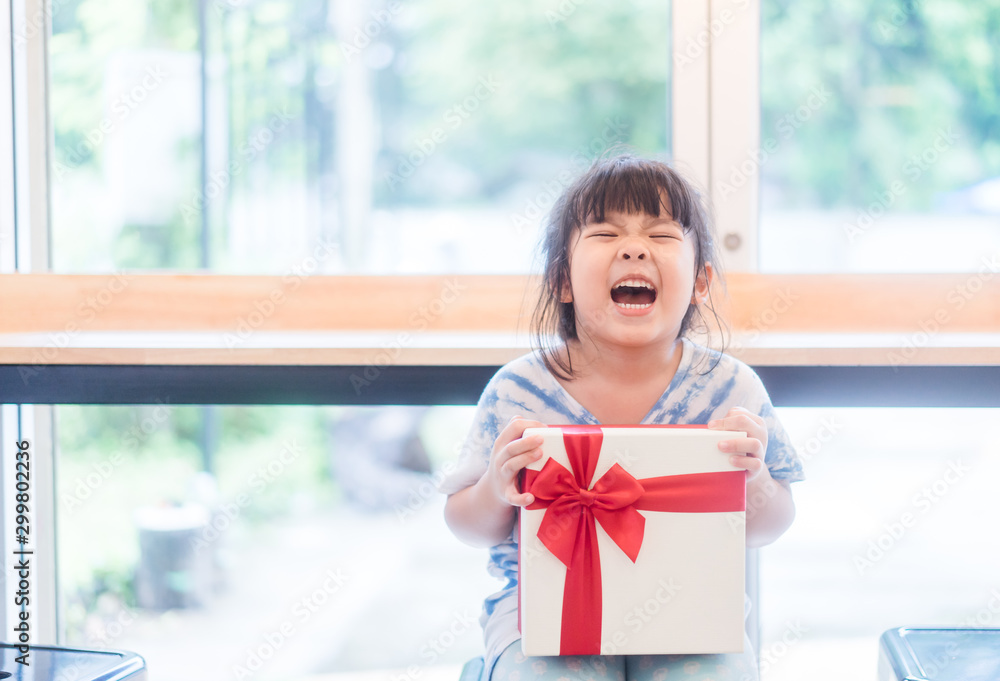 Little asian girl smile and excited and holding red gift box at home.child holding gift box in Christmas and New year concept. - obrazy, fototapety, plakaty 