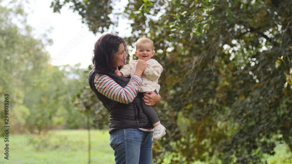 Young mother holds hugging her little baby child girl daughter walking spinning together in park nature Young mother holds hugging her little baby child girl daughter walking spinning together in park nature