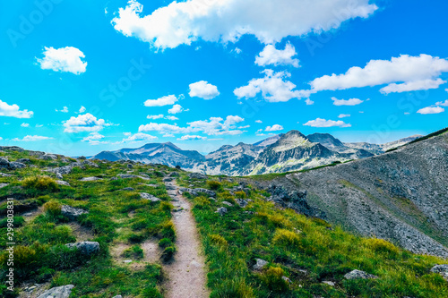 Amazing alpine mountain landscape, sunny hiking trail, grass and rocks, easy walk, but long way to go.