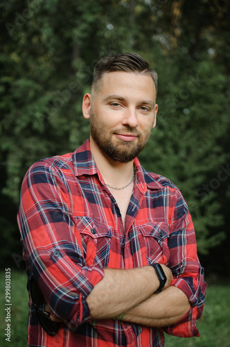 Outdoor portrait of relaxed handsome young man with beard in the park on green trees background. Hipster style concept.
