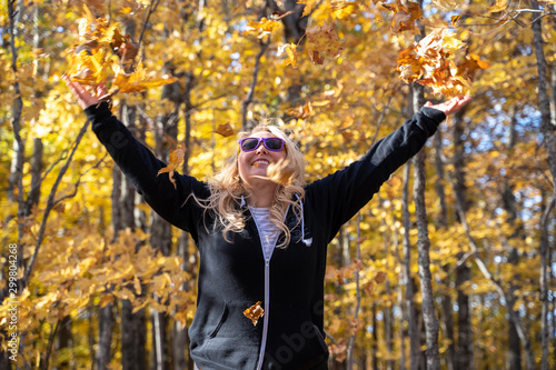 Joyful blond woman throws fall leaves in the air in a forest photo